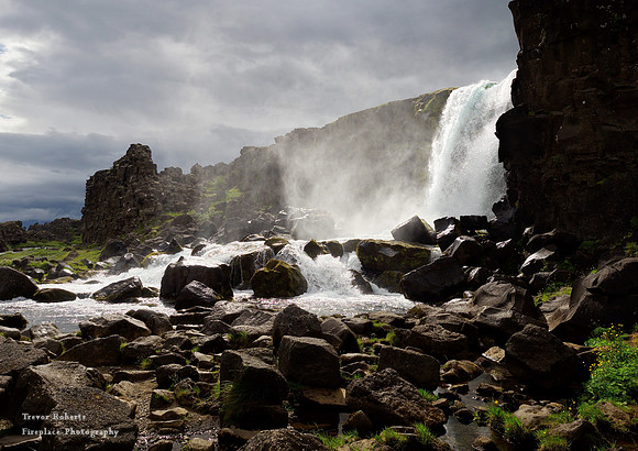 Waterfall catching the sunlight on a dark day at Þingvellir